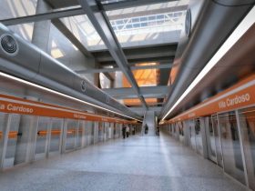 Projeção 3D do interior da futura estação Vila Cardoso da Linha 6 Laranja. A imagem mostra a plataforma central com as portas de plataforma nas laterais e a clarabóia permitindo entrada de luz no teto da estação.